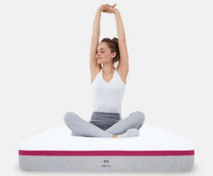 A woman sits cross-legged on a Helix mattress with her arms up.