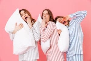 Portrait of sleeping women 20s in homewear having fun while resting at home together and yawning due to insomnia isolated over pink background.