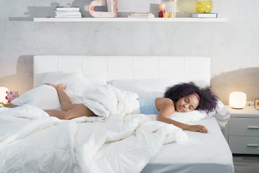 A woman lying on a white mattress with a white comforter.