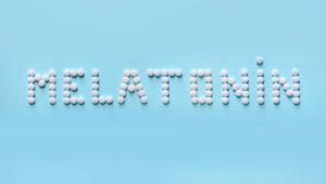The word "melatonin" spelled with pills against a light blue background.