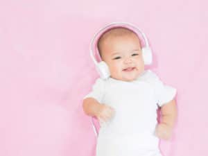 Blur hands of Asian baby girl wear white headphone and white shirt on pink background. Baby waves her hands aling the music from white headphones with sweet smile.; sleep music for babies concept.; lullabies for babies to sleep concept.