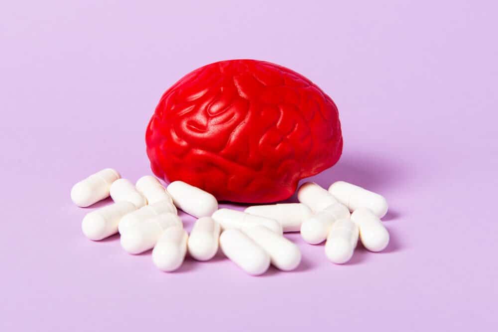 Red brain on a purple background with white pills. Some pills for the brain. Symbolic for drugs, psychopharmaceuticals, nootropics and other drugs. The medicine. Brain treatment.