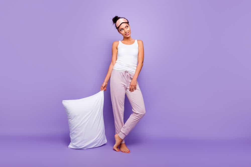A woman in pajamas standing against a purple wall while holding a memory foam pillow.