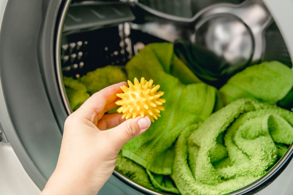 Using pvc dryer balls is natural alternative to both dryer sheets and liquid fabric softener, balls help prevent laundry from clumping in the dryer. Woman hand put in a yellow spiky dryer ball.