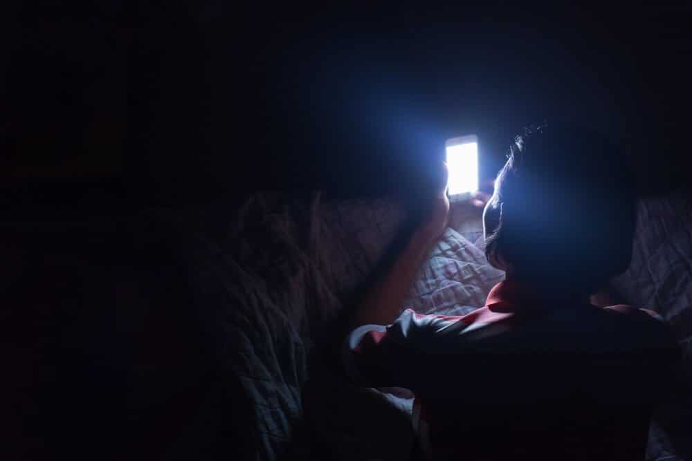 Asian young man using his mobile phone on the bed in dark room. Thin guy playing his smartphone on the bed in dark room.