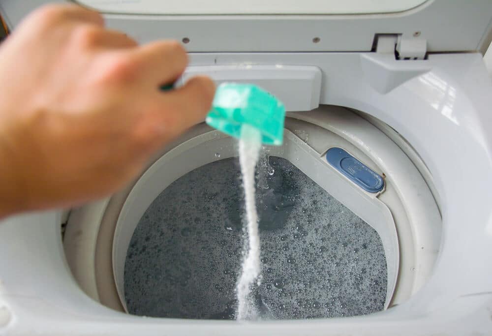 Person adding baking soda into washing machine to wash clothes for brighter and cleaner finish