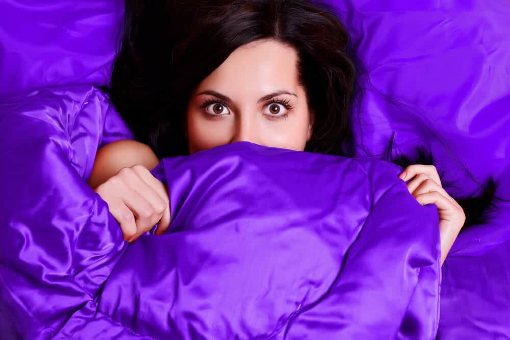 A woman hides her face behind bright purple organic bed sheets.