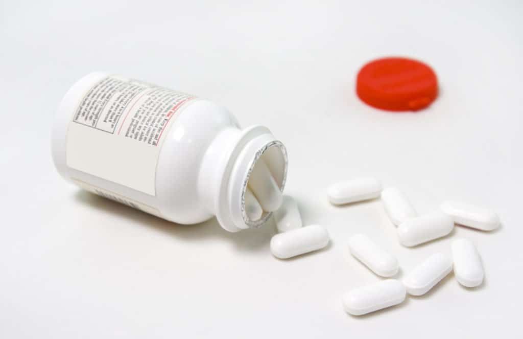 A white pill bottle with a red cap spilling white pills on a white counter.