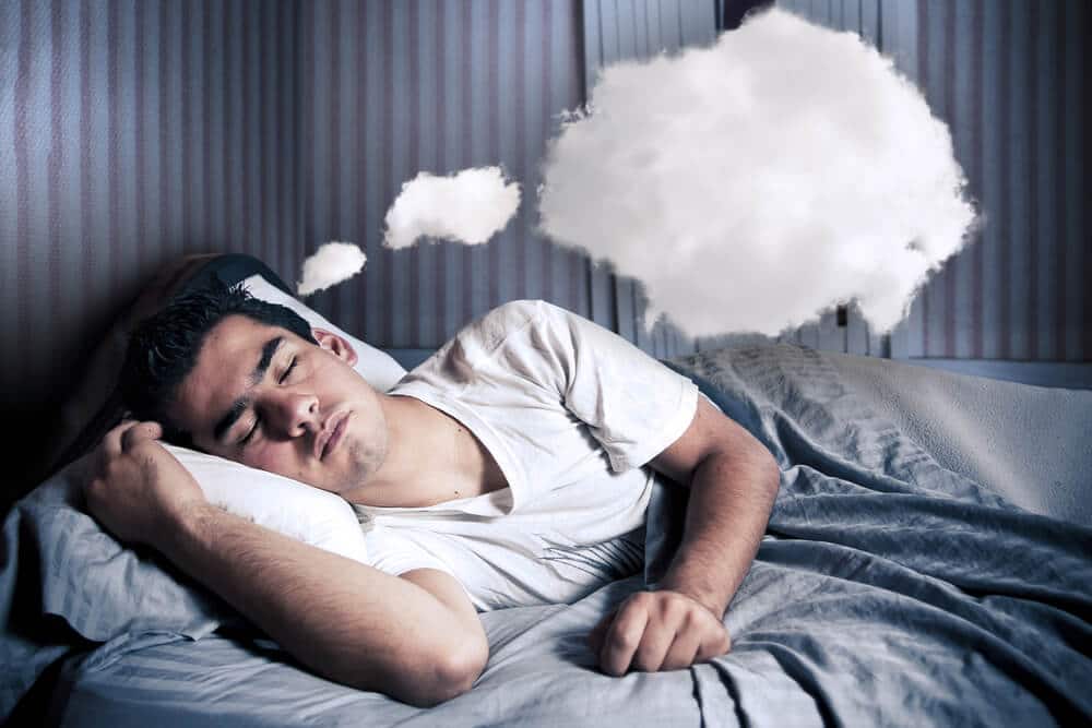 Man comfortably sleeping in his bed at night, with clouds above his head to indicate dreams.
