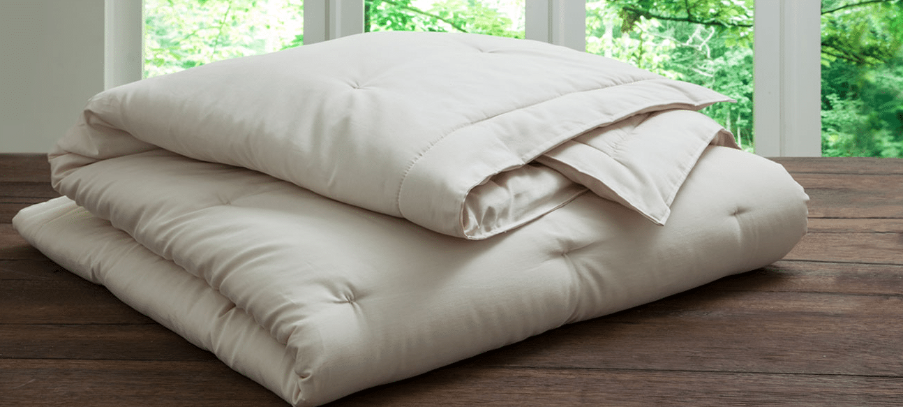 A folded handmade comforter from PlushBeds rests on a wooden surface.