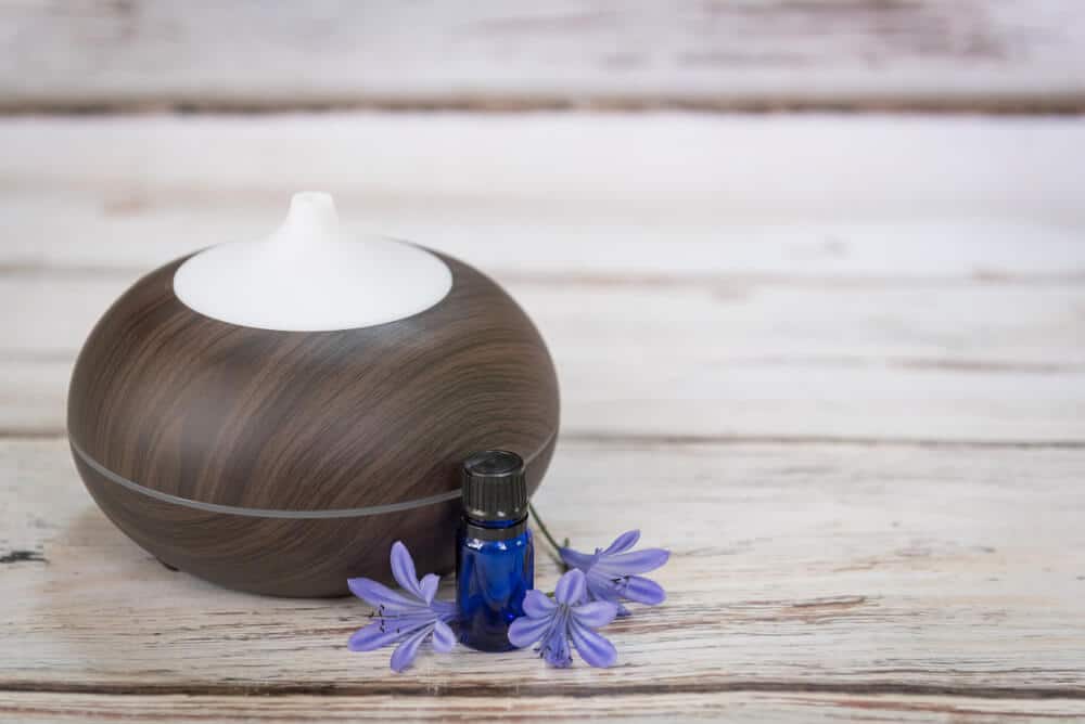 Oil diffuser and blue bottle of oil on the white wooden floor with flowers and bracelet.
