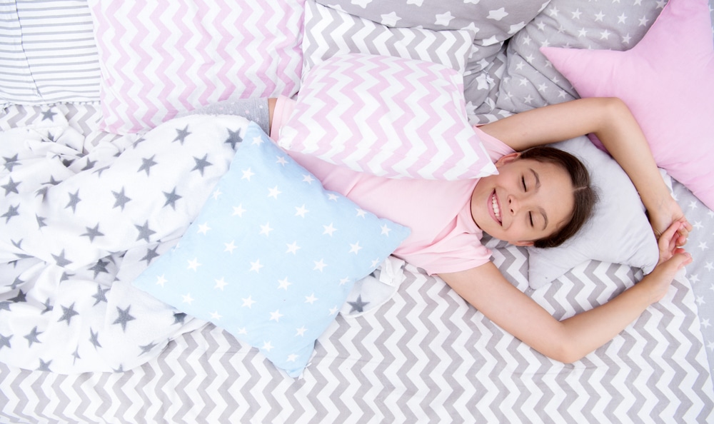 A girl sleeping on flannel sheets with throw pillows and a blanket.