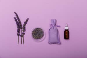 Essential lavender oil and flower with small bag on purpule background. Wellness with lavender, minimal concept. Beauty treatment top view.
