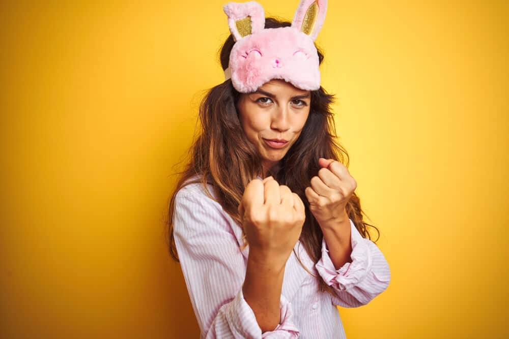 Young woman wearing pajama and sleep mask standing over yellow isolated background Ready to fight with fist defense gesture, angry and upset face, afraid of problem