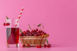 Tart cherry juice in a glass and pitcher on pink with ripe berries in wicker basket