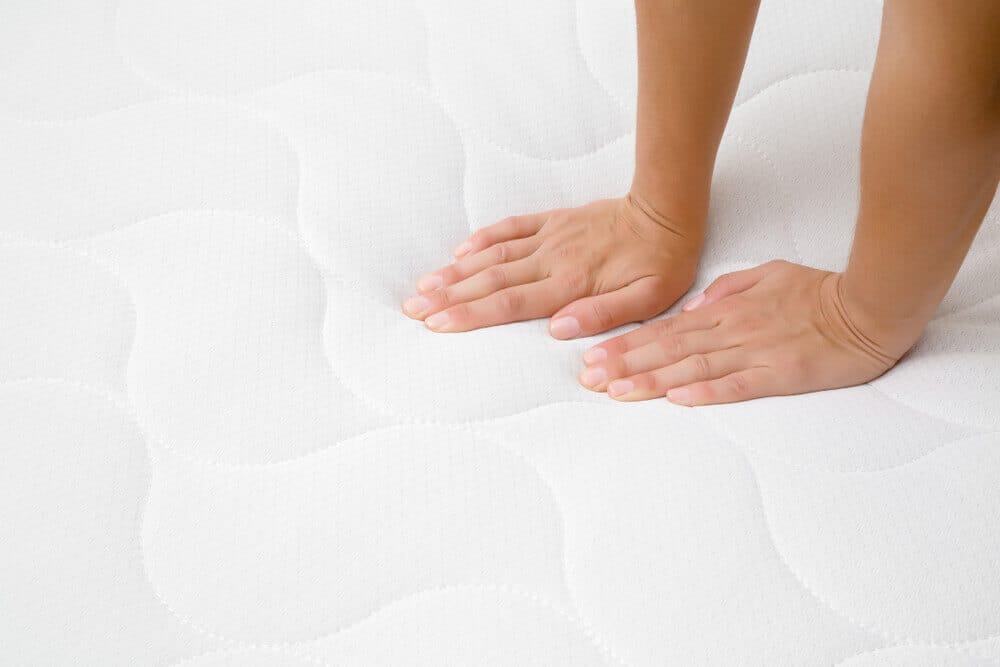 Woman's hands pressing on white mattress. Checking hardness and softness. Choice of the best type and quality. Side view. Close up.