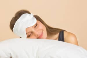 beautiful young woman on a beige background in a sleep mask with a pillow in her hands