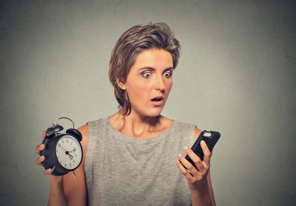 Young woman with mobile phone and alarm clock stressed running late