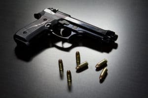 A black gun with five bullets sitting on a surface.