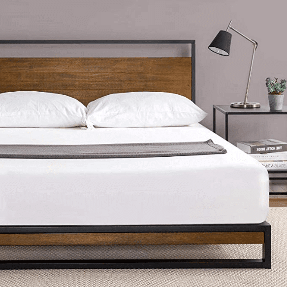 A wood and metal bed frame with white bed sheets and two white bed pillows and a brownish gray throw blanket.