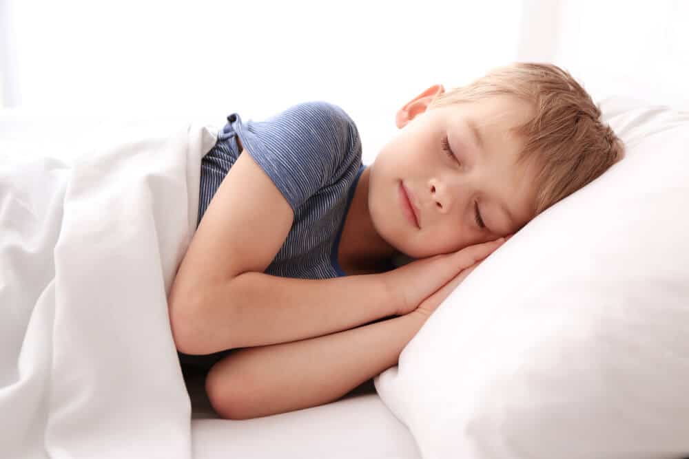 A child in a blue shirt sleeping on a white pillow with a white blanket.
